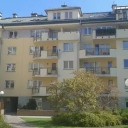 Elewacja wielorodzinnego budynku z balkonami, widok z poziomu trawnika z drzewami i krzewami