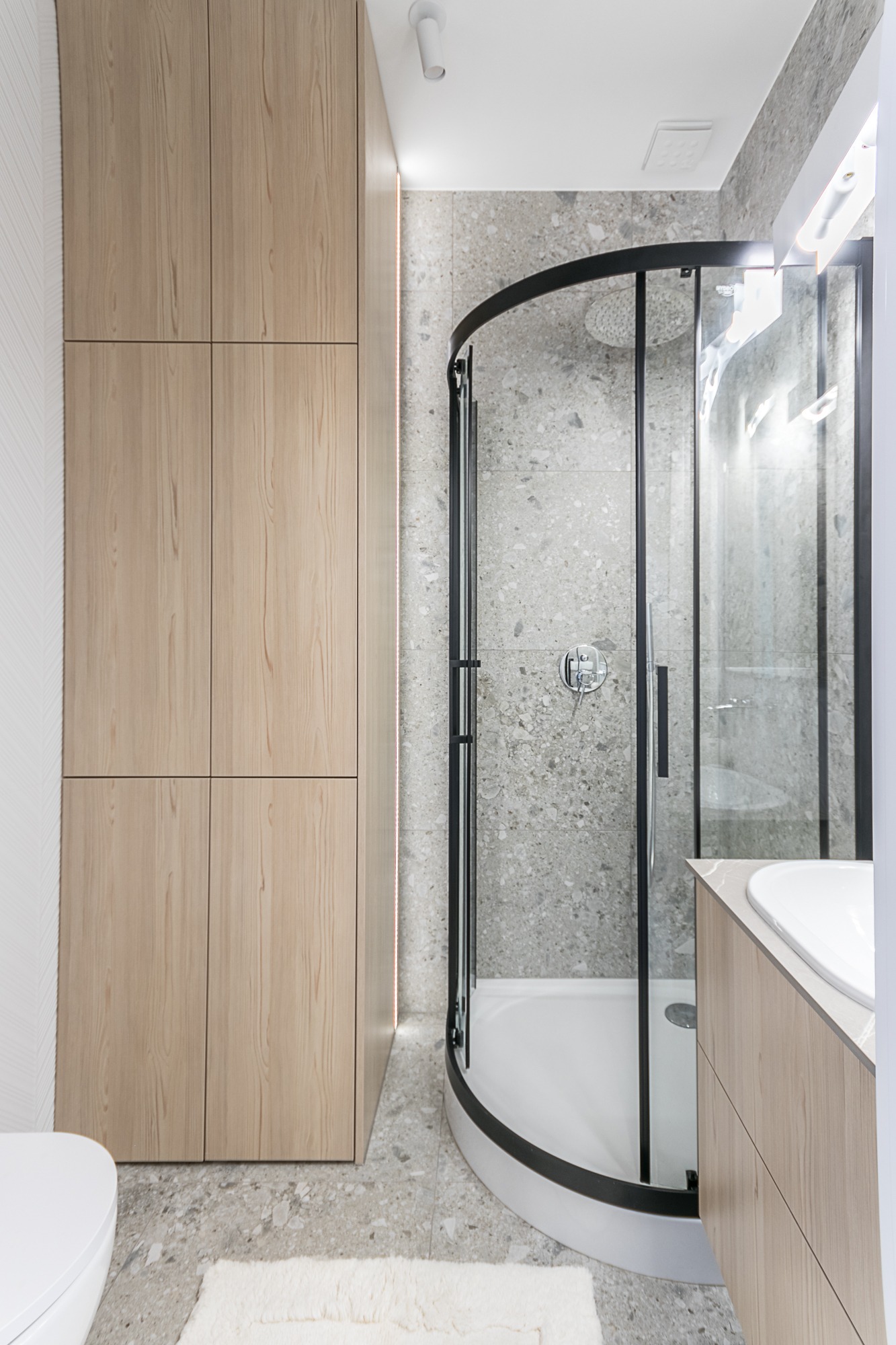 Nowoczesna łazienka z kabiną prysznicową z czarnymi ramami, szafką z jasnego drewna i szarą mozaiką na ścianach. Minimalistyczny design.