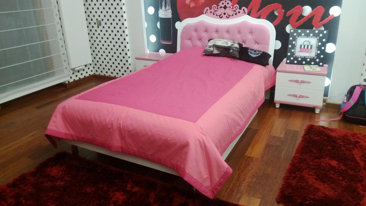 Różowe łóżko z pikowanym zagłówkiem w pokoju dziewczynki, widoczne szafki nocne i dywan w kolorze burgundu.