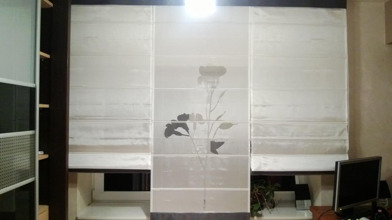 Trzyczęściowa, kremowa roleta rzymska z motywem kwiatowym na środkowym panelu, widoczna w oknie pokoju z biurkiem i komputerem.