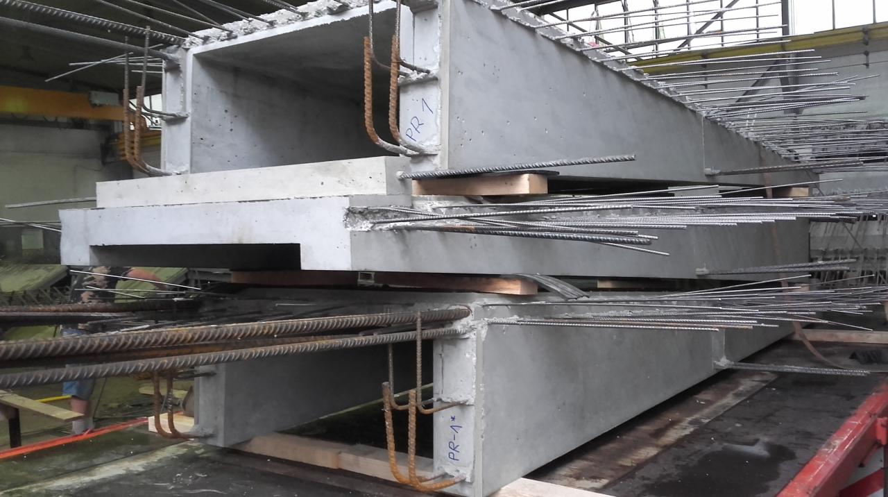 Magazyn prefabrykowanych, żelbetowych elementów konstrukcyjnych, z wystającymi prętami zbrojeniowymi i oznaczeniem 'PR-A*', ułożonych warstwami na drewnianych podkładkach.