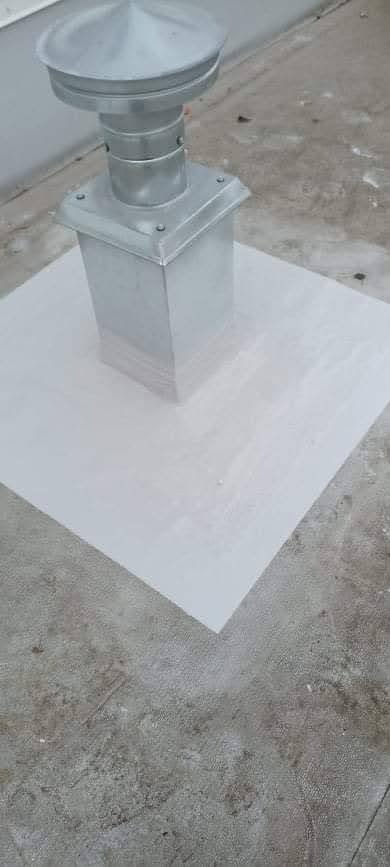 Metalowy komin na dachu, zabezpieczony białą powłoką hydroizolacyjną, widoczne ślady zabrudzeń na powierzchni dachu.