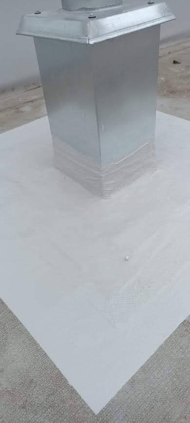 Metalowy komin na dachu zabezpieczony białą powłoką hydroizolacyjną, z widocznymi śladami pędzla i taśmą uszczelniającą u podstawy.