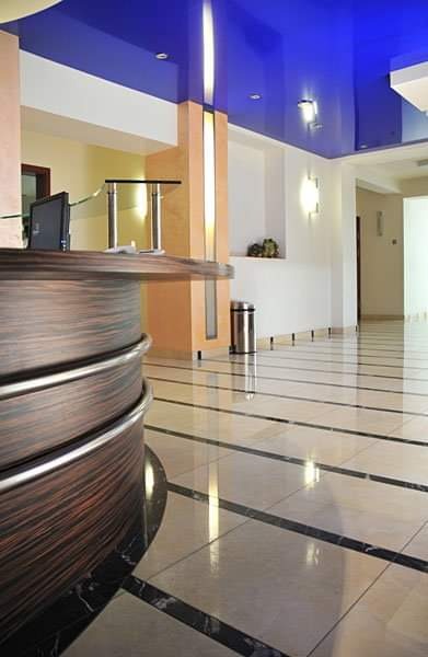 Błyszcząca podłoga z płytek w holu recepcyjnym z ciemnymi fugami i niebieskim sufitem podwieszanym.