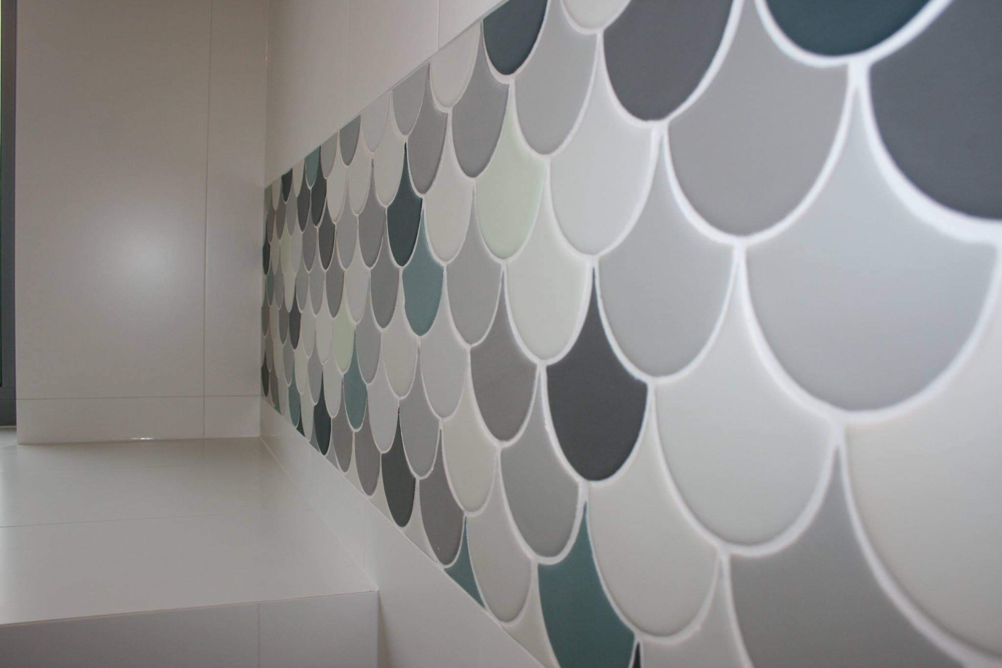 Ściana wyłożona mozaiką w kształcie rybiej łuski w odcieniach szarości, bieli i turkusu, zakończona białą fugą, z widocznym fragmentem białej ściany i podłogi.