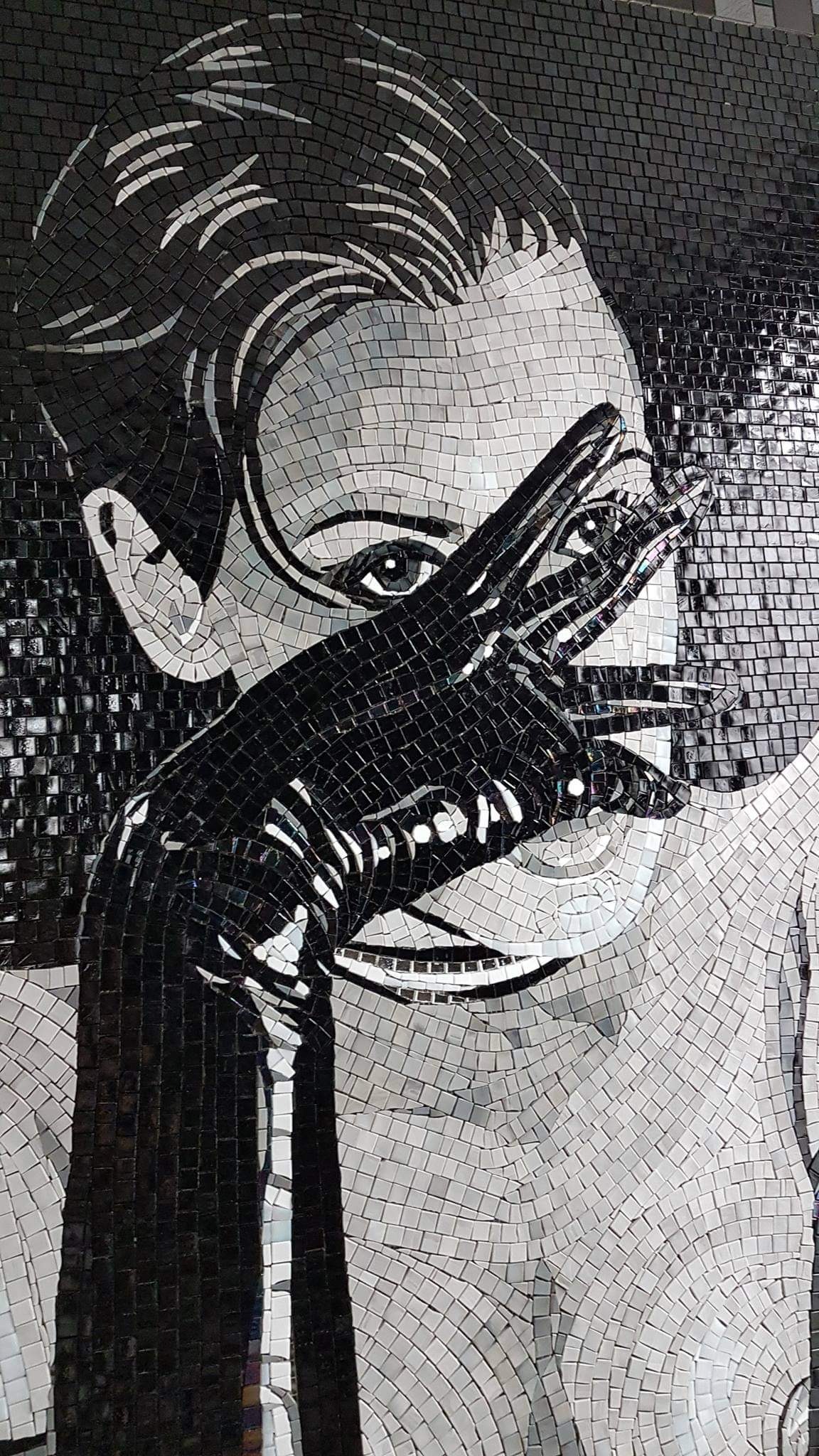 Mozaika przedstawiająca portret kobiety w stylu retro, z rękawiczką zasłaniającą część twarzy, wykonana z czarno-białych płytek o kwadratowym kształcie.