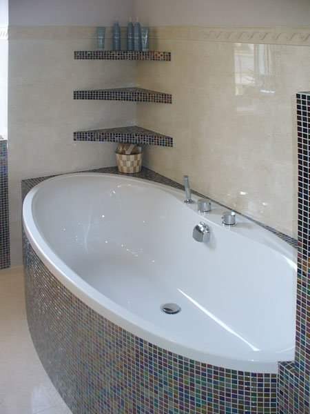 Nowoczesna łazienka z owalną wanną obłożoną mozaiką w odcieniach niebieskiego, zieleni i brązu, z półkami narożnymi wykończonymi identyczną mozaiką.