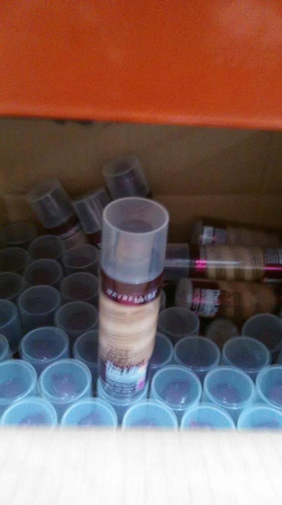 Partia nowych podkładów w płynie marki Maybelline, zapakowanych w plastikowe pojemniki z przezroczystymi wieczkami, widoczna w kartonowym pudle.