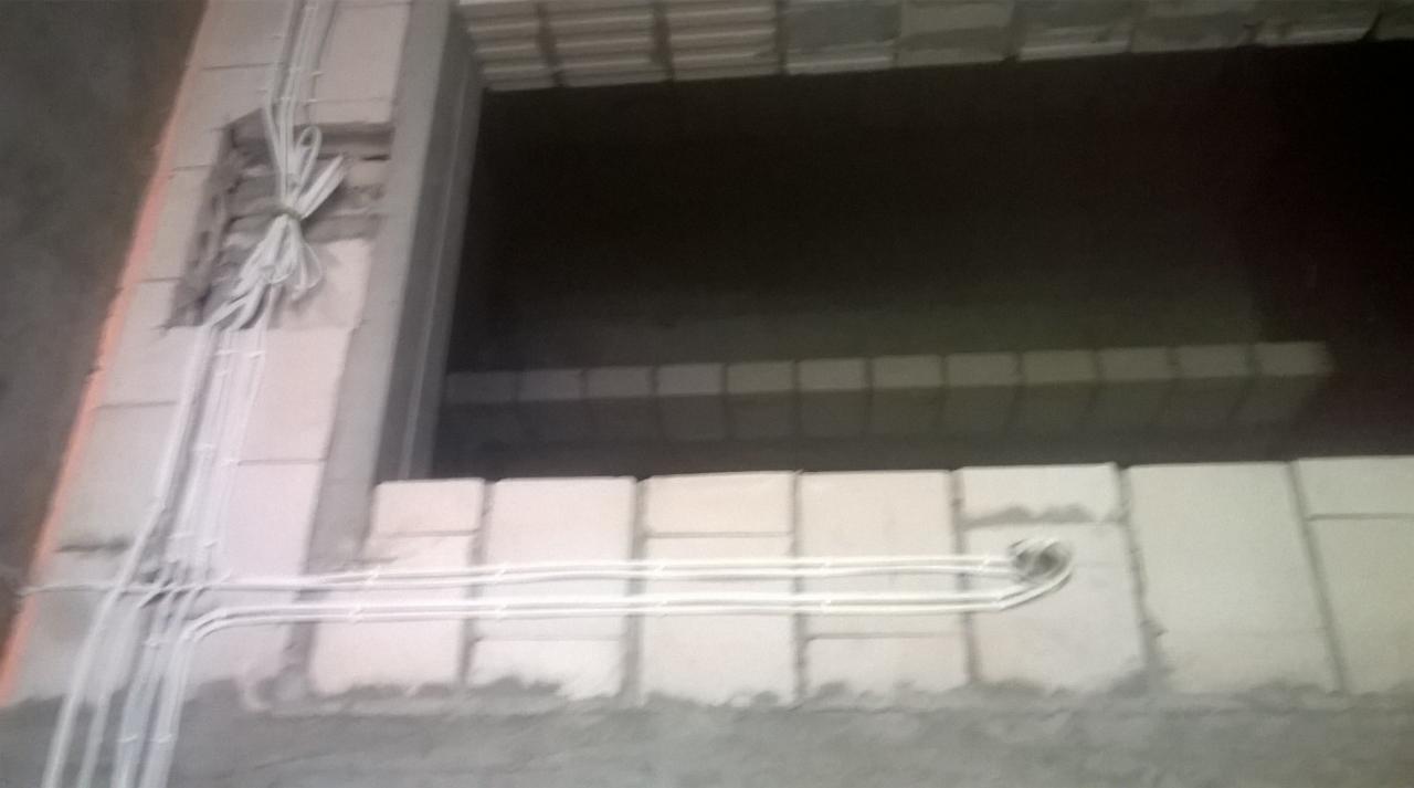 Białe przewody poprowadzone wzdłuż ściany z betonu komórkowego na budowie, widoczne mocowania i wiązka przewodów wychodząca ze ściany.