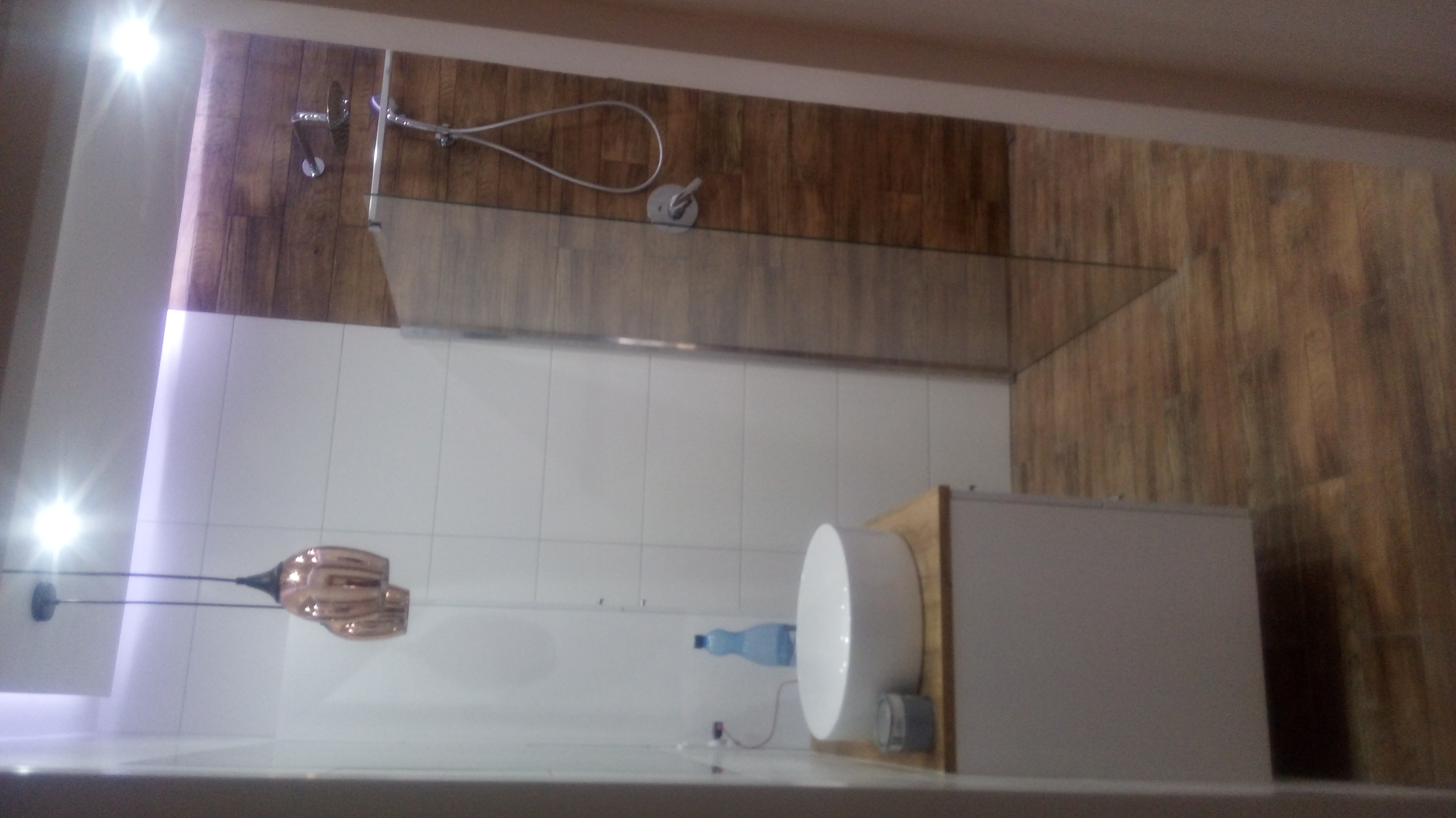 Wykończona łazienka z kabiną prysznicową typu walk-in, białą umywalką nablatową, drewnopodobnymi płytkami na ścianach i suficie oraz wiszącą lampą w kolorze miedzi.