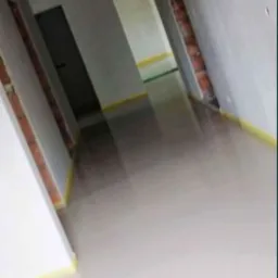 Świeżo wylana, jasna posadzka w korytarzu z widocznymi fragmentami ścian z cegły i taśmą zabezpieczającą przy podłodze.