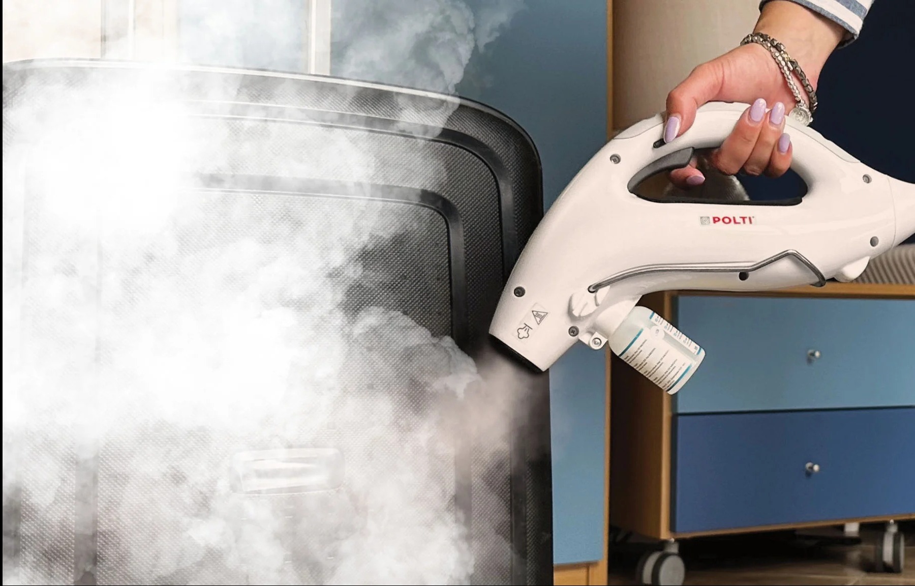 Dezynfekcja parowa szafy przez osobę z fioletowymi paznokciami, używającą parownicy Polti z dołączonym pojemnikiem na płyn dezynfekujący.