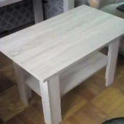 Niski, prostokątny stolik kawowy z jasnego drewna z półką, ustawiony na parkiecie w pokoju.