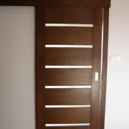 Ciemnobrązowe przesuwne skrzydło z czterema podłużnymi, poziomymi prześwitami, zamontowane w ościeżnicy, widoczne na tle szarej i białej ściany oraz drewnianej podłogi.