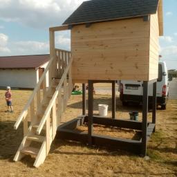Zakład Stolarski Wojciech Krawiec - Drewniany domek dla dzieci z drabinką i piaskownicą, świeżo po montażu, z widocznymi śladami farby i pojazdem dostawczym w tle.