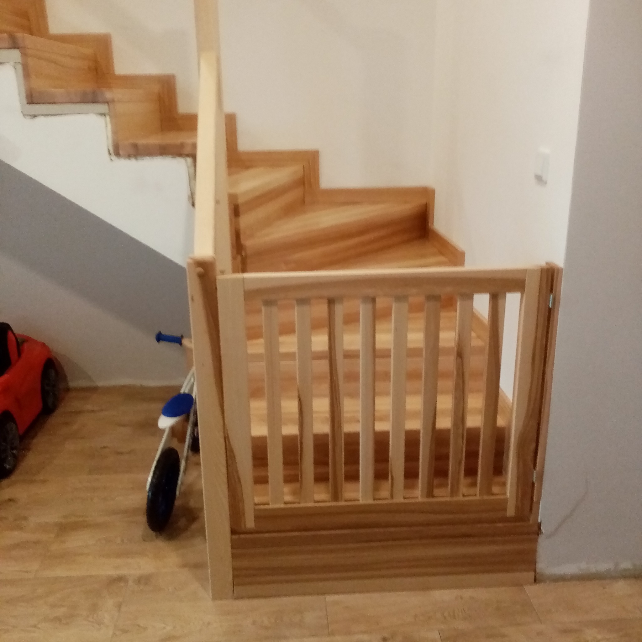 Drewniane schody z barierką zabezpieczającą dla dzieci, wykonane w Rydzynie. Widoczny rowerek i autko dziecięce, co sugeruje domowy charakter realizacji.