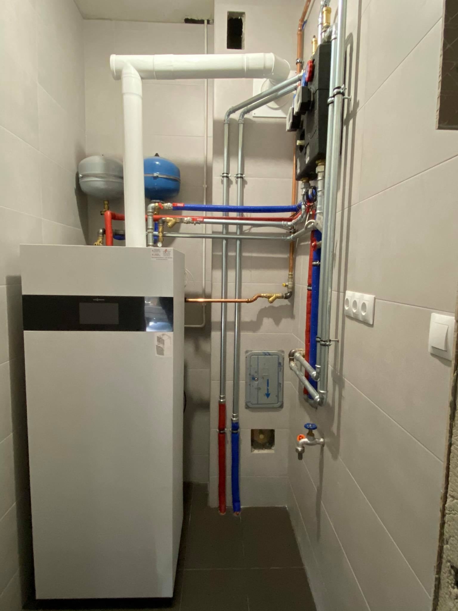 Nowoczesny piec gazowy Viessmann z podłączeniami hydraulicznymi w schludnej kotłowni z szarymi płytkami, widoczne rury miedziane i plastikowe w kolorach czerwonym i niebieskim, oraz zawory...