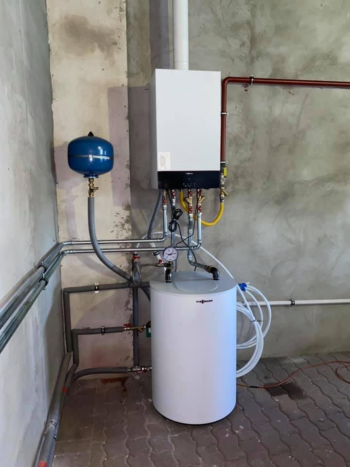 Nowo zainstalowany, wiszący piec gazowy Viessmann z podłączonym zasobnikiem ciepłej wody i niebieskim naczyniem przeponowym, widoczne rury miedziane i instalacja hydrauliczna, surowy beton...