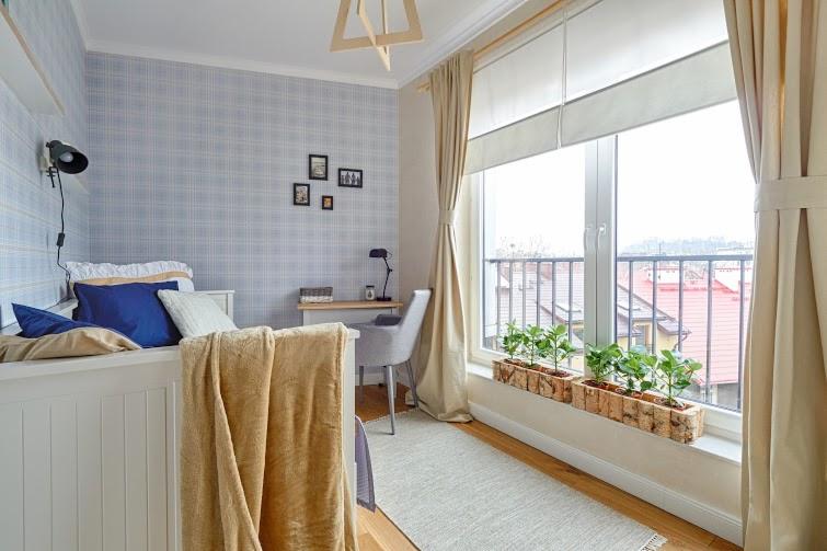 Pokój dziecięcy z łóżkiem, biurkiem i oknem balkonowym z roślinami w doniczkach z kory brzozowej, tapeta w kratę, drewniana lampa sufitowa.