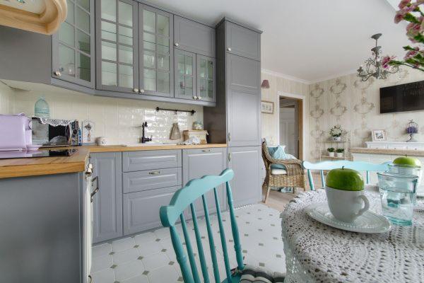 Szara kuchnia w stylu rustykalnym z turkusowymi krzesłami w Bibicach. Na stole jabłka w filiżance i szklanki z wodą.