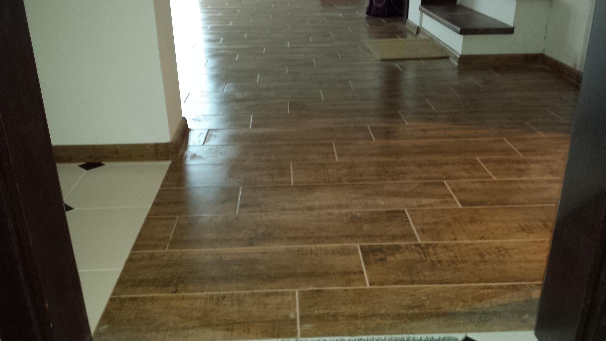 Ułożona podłoga z brązowych paneli imitujących drewno, widoczne fugi i fragment progu z płytkami w rogu pomieszczenia.