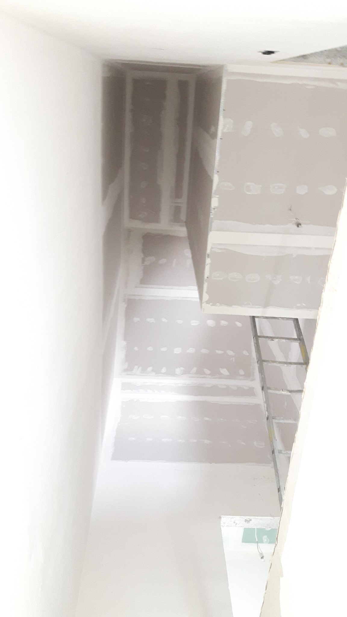 Sufit z zamontowanymi płytami gipsowo-kartonowymi, widoczne łączenia i ślady po wkrętach, częściowo oświetlony drabiną aluminiową.