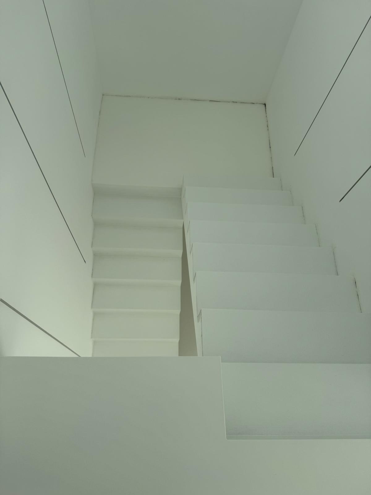 Minimalistyczne, białe schody betonowe widziane z góry, z ciemnymi liniami dekoracyjnymi na ścianach.