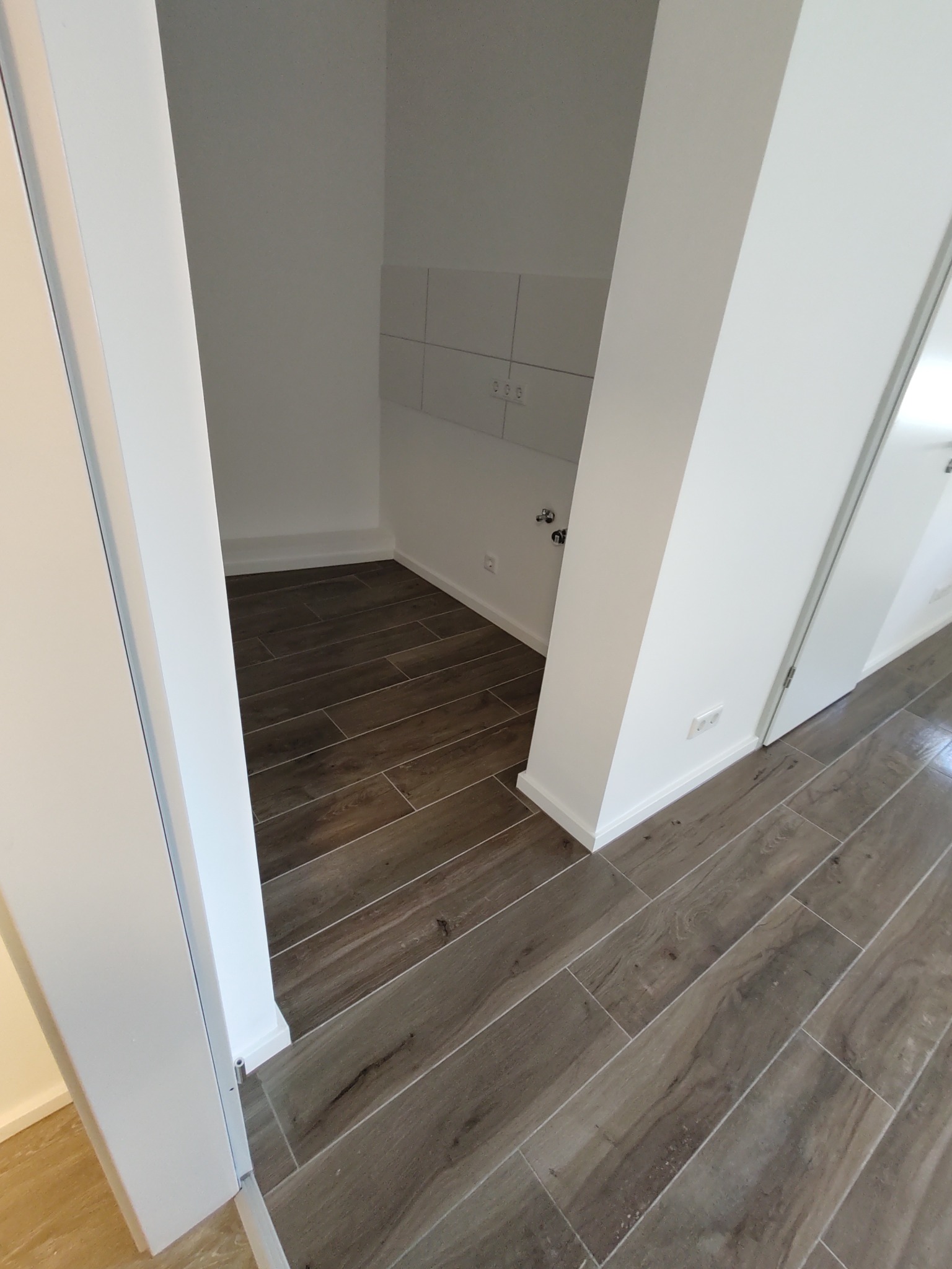 Wnęka w nowym mieszkaniu z podłogą wyłożoną płytkami imitującymi drewno i świeżo pomalowanymi na biało ścianami.