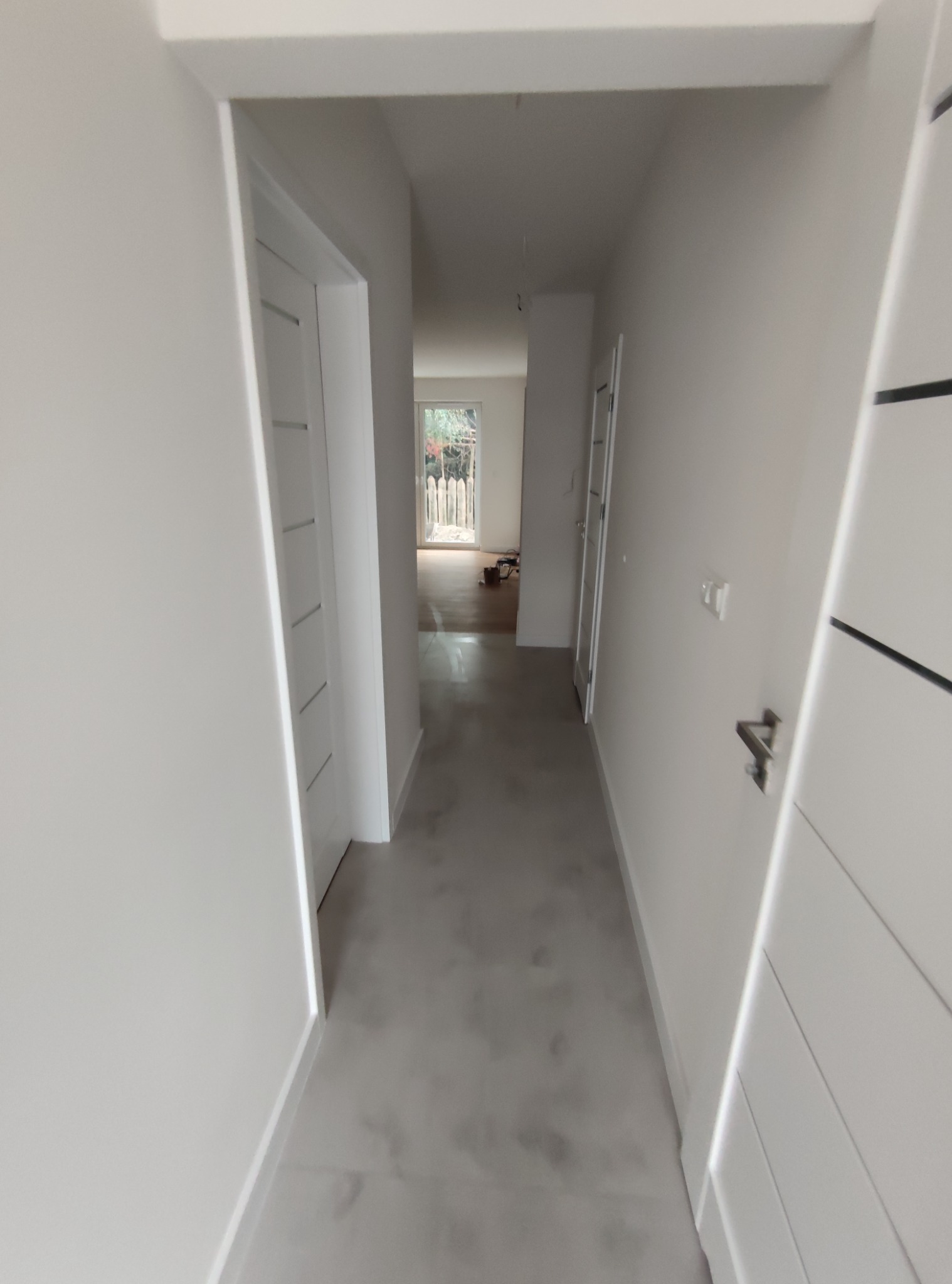 Wnętrze korytarza z białymi ścianami i drzwiami, widok w głąb mieszkania, widoczne wykończone podłogi i świeżo pomalowane ściany.