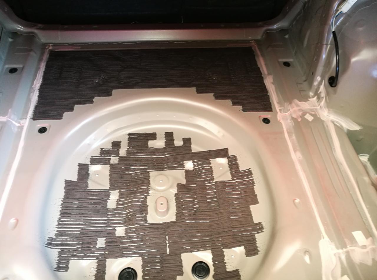 Bagażnik samochodu po nałożeniu wygłuszenia w formie pasków, widoczne niedokładności i puste przestrzenie.