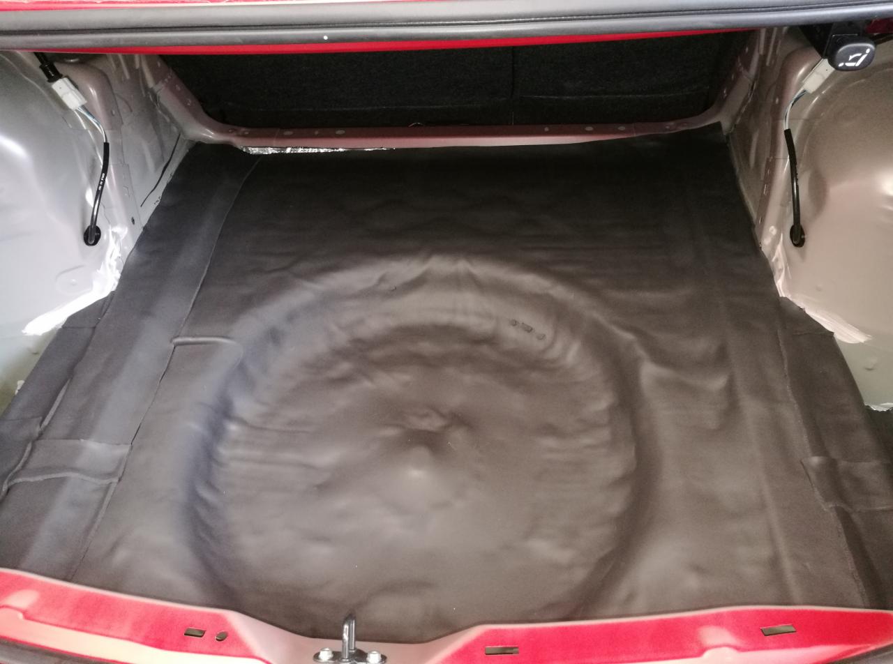 Wyłożony materiałem bagażnik samochodu z widocznym miejscem na koło zapasowe.