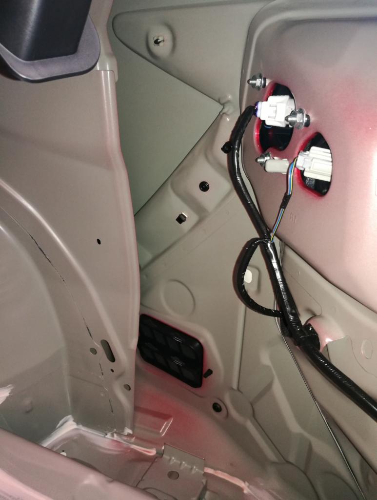 Wnętrze bagażnika samochodu z widocznymi przewodami i mocowaniami lamp tylnych, prawdopodobnie w trakcie montażu lub naprawy.