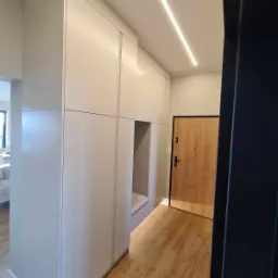 Wnętrze przedpokoju z zabudową szafy na wymiar w kolorze jasnoszarym, z wnęką do siedzenia, oświetleniem LED na suficie i drewnianą podłogą.