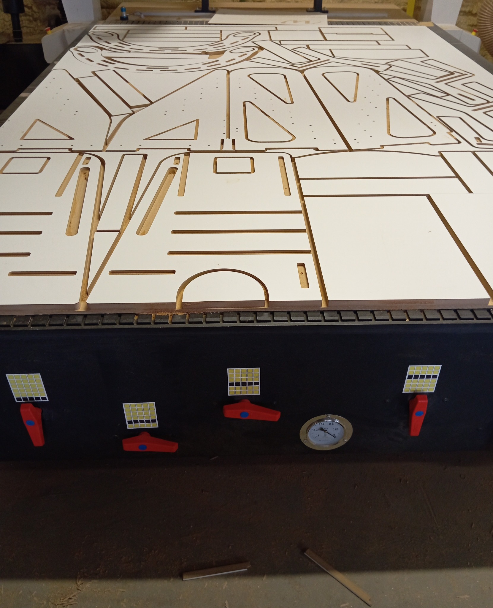 Płyta MDF z wyfrezowanymi elementami na stole roboczym frezarki CNC, widoczne detale i otwory, przygotowane do dalszej obróbki.