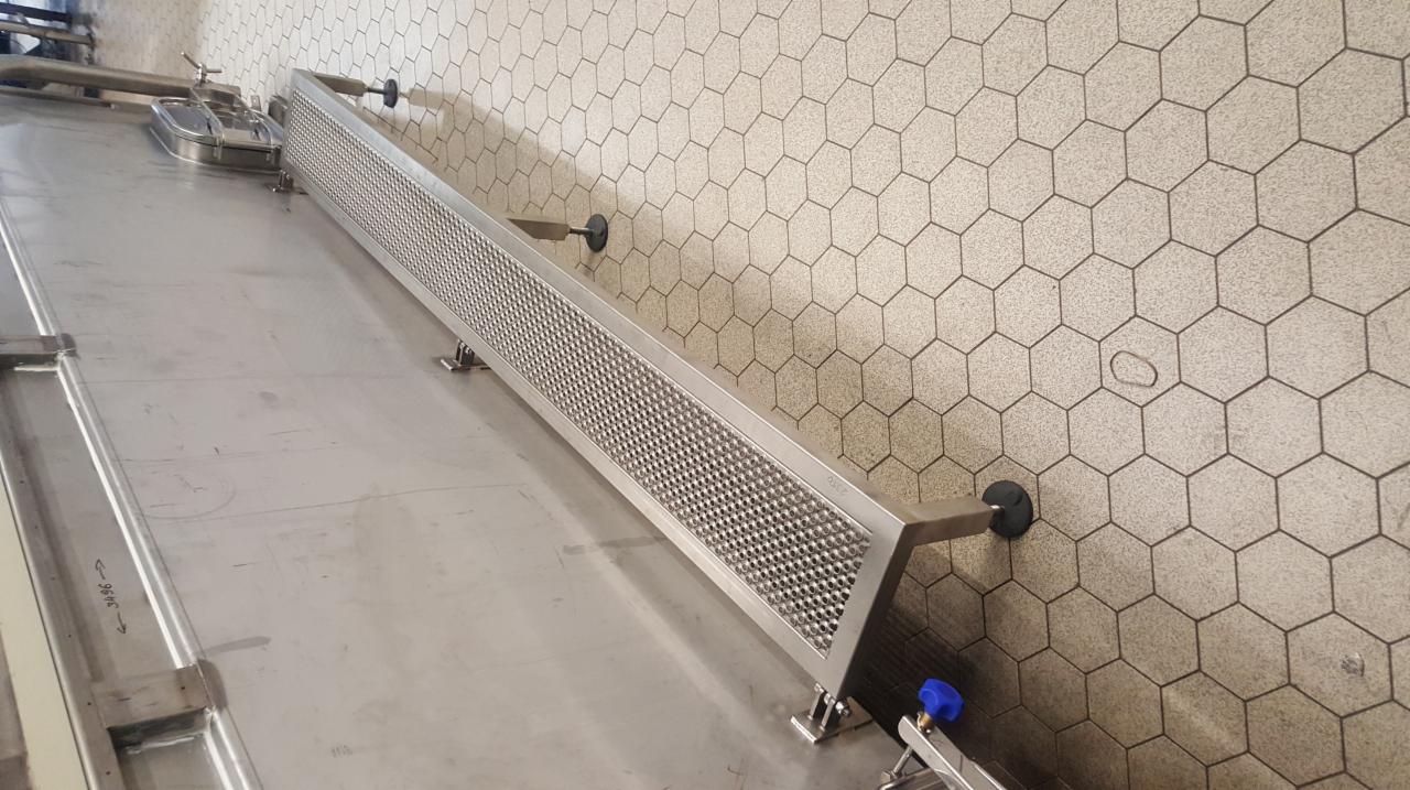 Metalowa konstrukcja z perforowaną powierzchnią i elementami mocującymi, umieszczona przy ścianie z heksagonalnymi płytkami.