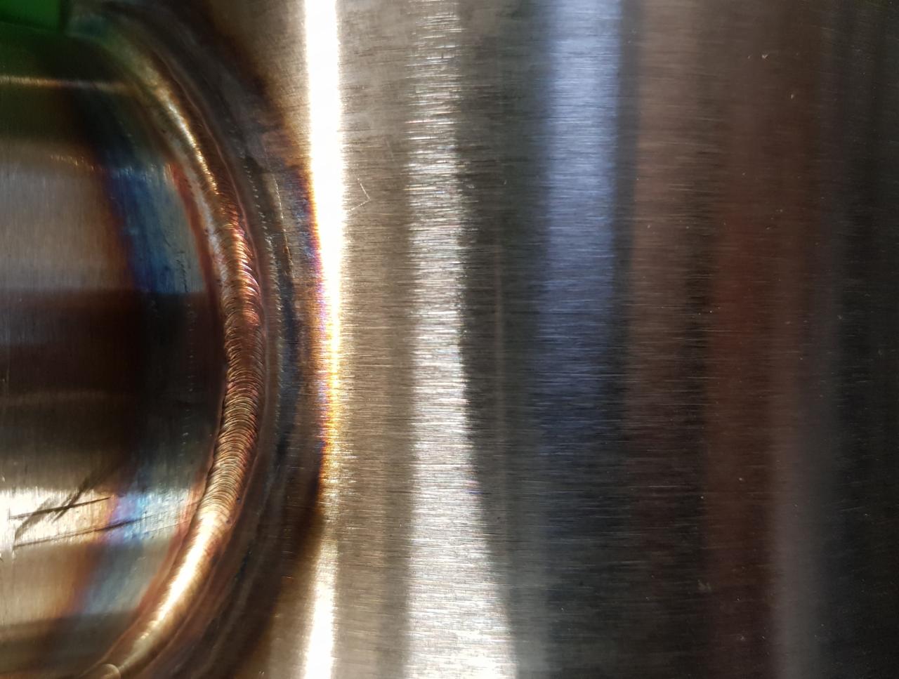 Metalowa powierzchnia po spawaniu z widocznymi śladami wysokiej temperatury i zmianami koloru wzdłuż spoiny.