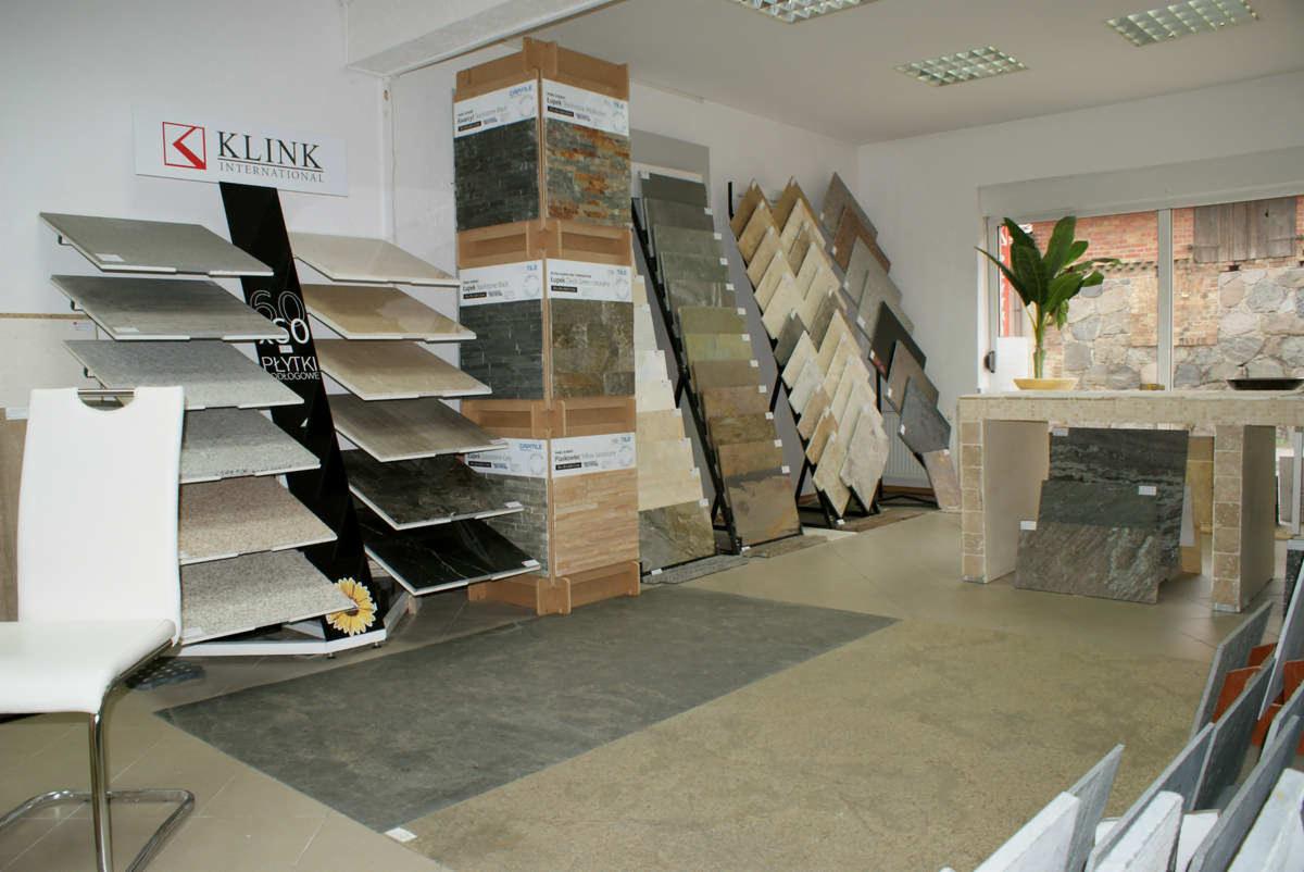 Ekspozycja różnorodnych płytek podłogowych i ściennych w salonie, prezentująca różne wzory, kolory i tekstury, z logo 'KLINK INTERNATIONAL' widocznym na jednym ze stojaków.