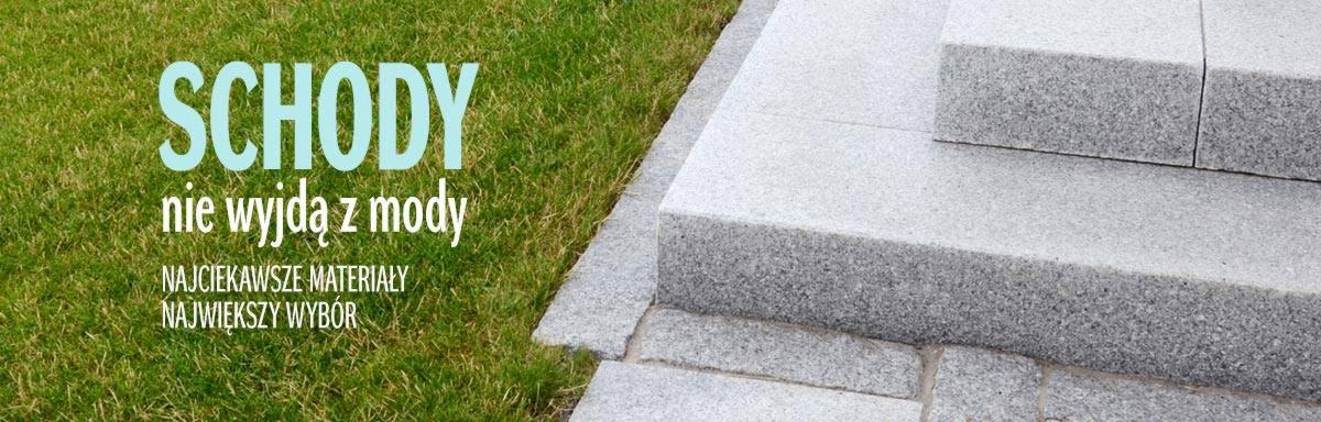 Schody zewnętrzne z jasnoszarego kamienia, obok trawnik; na zdjęciu widoczny napis reklamowy.