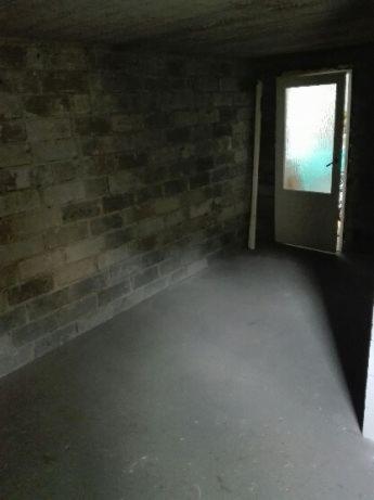Surowe wnętrze piwnicy z surowymi ceglanymi ścianami i betonową podłogą, widoczne drzwi z matową szybą w tle.