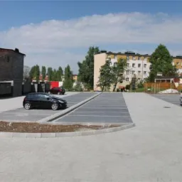 Ukończony parking z kostki brukowej w Andrychowie, z dwoma samochodami i białym vanem na tle budynków mieszkalnych.