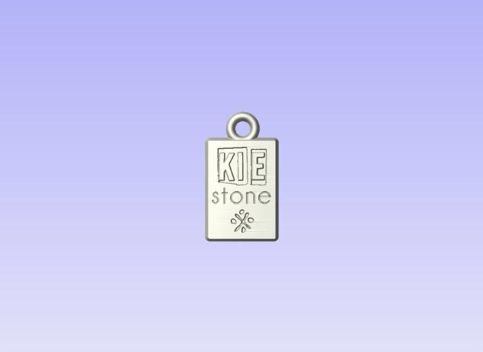 Metalowy brelok z grawerowanym napisem 'KIE stone' i symbolem kwiatka, zawieszka z kółkiem na górze, na jednolitym tle.