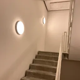 Betonowe schody w klatce schodowej z białymi poręczami i okrągłymi lampami ściennymi