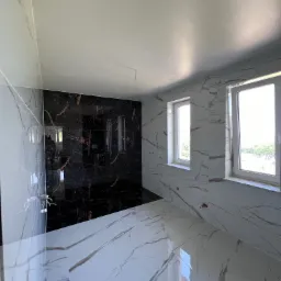 Wykończona łazienka w Jodłowniku z czarno-białymi płytkami imitującymi marmur, widoczne dwa okna z białymi ramami.