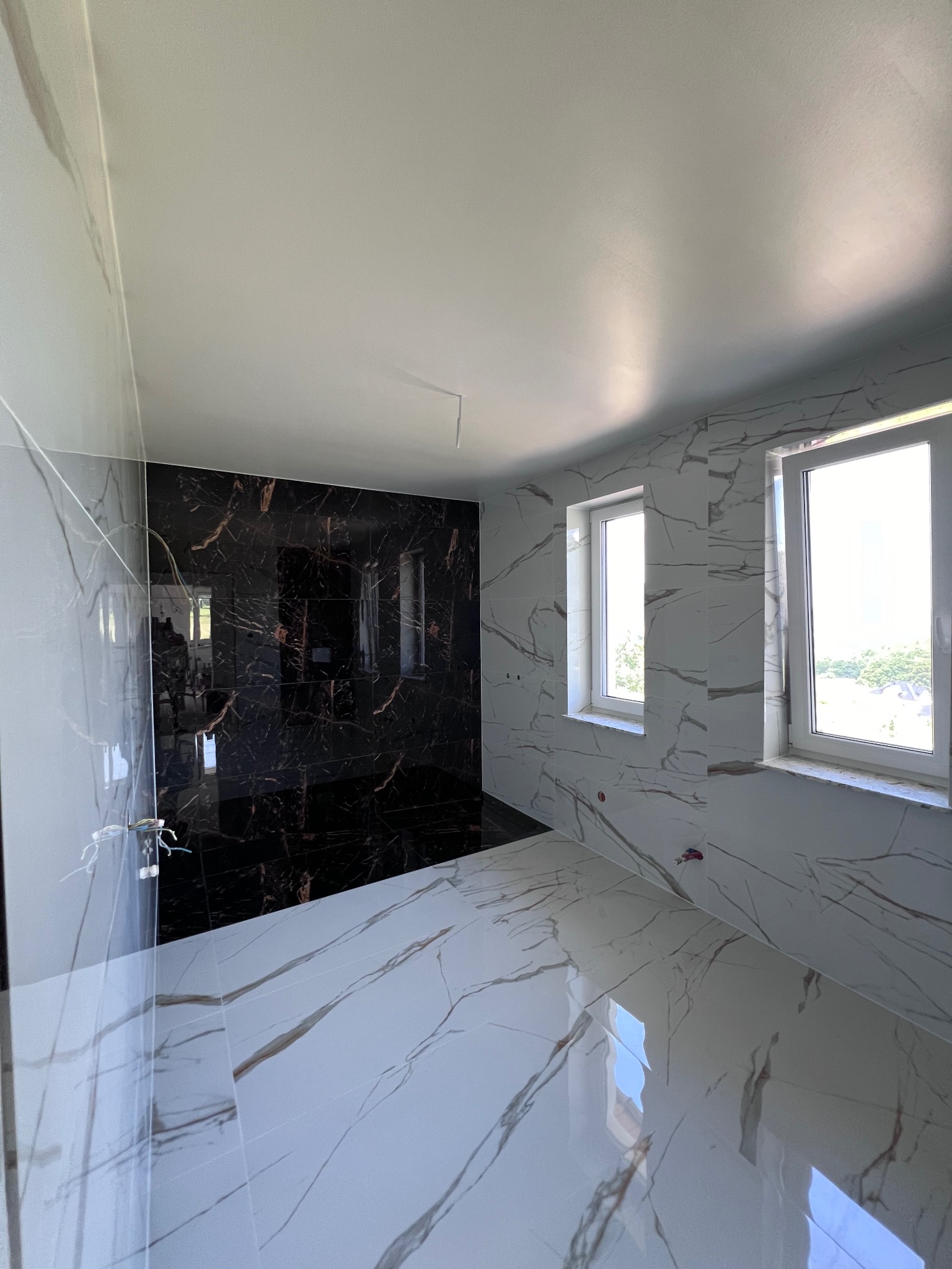 Wykończona łazienka w Jodłowniku z czarno-białymi płytkami imitującymi marmur, widoczne dwa okna z białymi ramami.