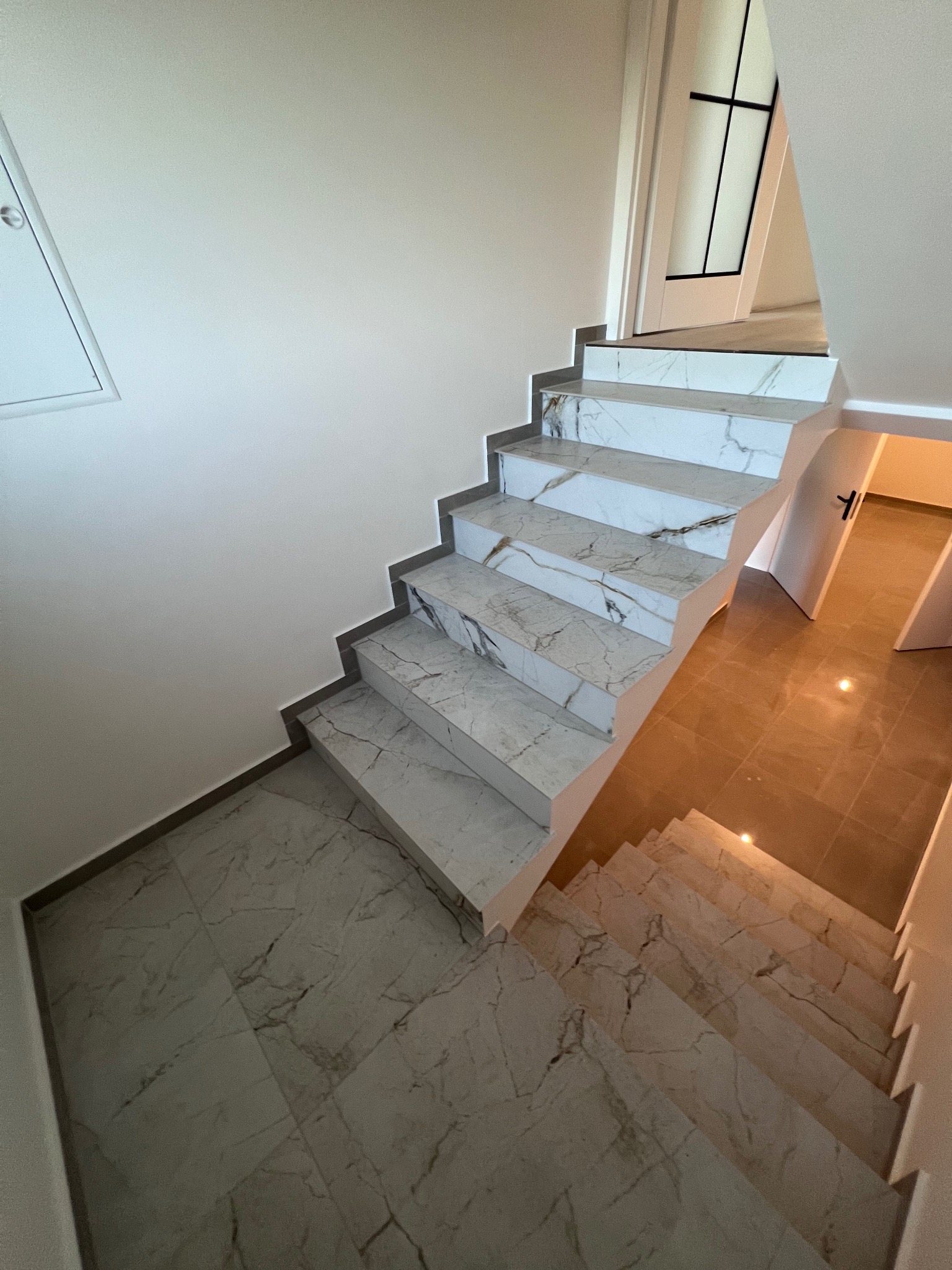 Wykończone schody wewnętrzne z marmurowymi płytkami, dopasowane do podłogi w holu, widok z góry na dół.