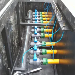 Instalacja z rzędami rur z zaworami i przewodami w czarnej skrzyni, prawdopodobnie system nawadniania lub drenażu, widok z góry.