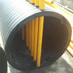 Duża, czarna, karbowana rura z żółtymi rurami wewnątrz, prawdopodobnie element instalacji podziemnej.