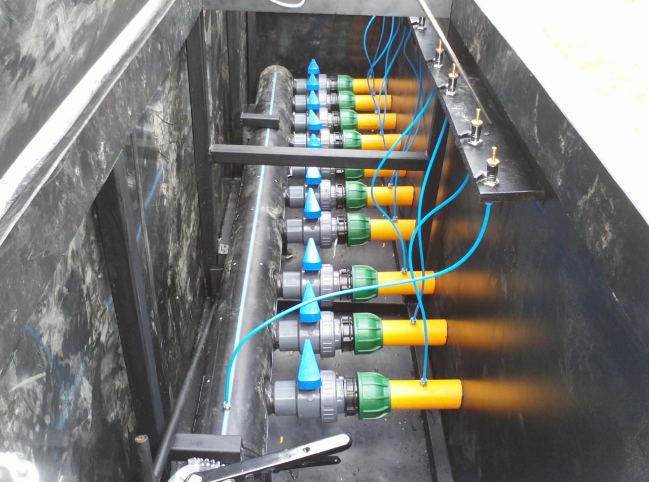 Instalacja z rzędami rur z zaworami i przewodami w czarnej skrzyni, prawdopodobnie system nawadniania lub drenażu, widok z góry.