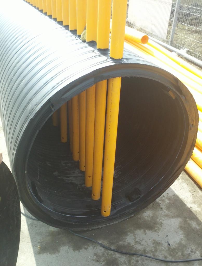 Duża, czarna, karbowana rura z żółtymi rurami wewnątrz, prawdopodobnie element instalacji podziemnej.