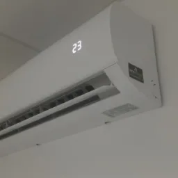 Biała klimatyzacja ścienna z wyświetlaczem temperatury 23 stopnie Celsjusza, zamontowana na jasnej ścianie.